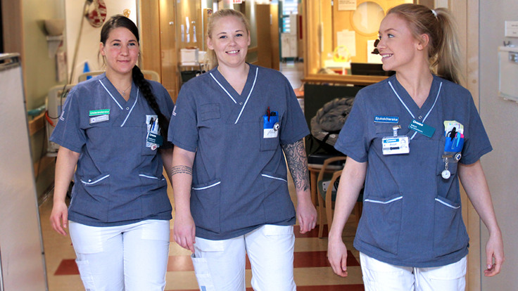 Tre kvinnor i vårdkläder går i en korridor