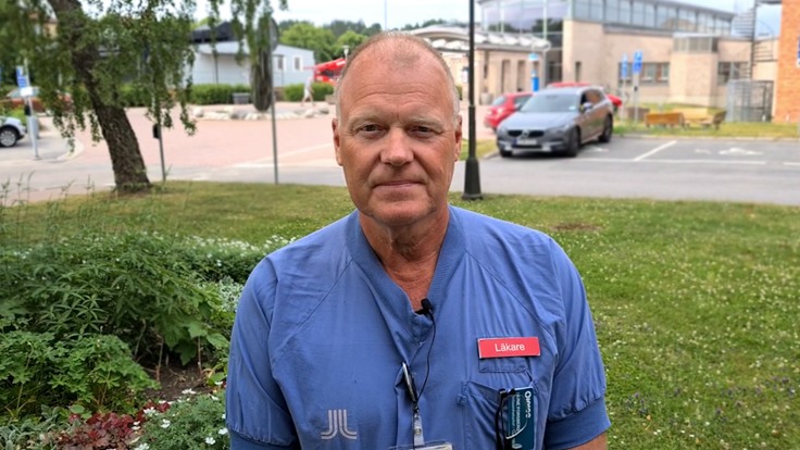 Man i sjukvårdskläder framför sjukhusbyggnad.