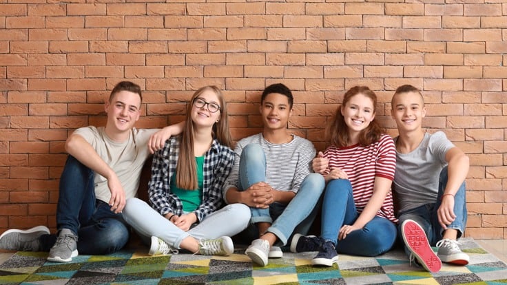 Grupp med ungdomar sitter på golvet vid en tegelvägg.