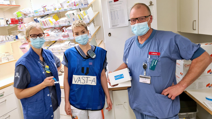 Tre vårdklädda medarbetare med munskydd i läkemedelsförråd