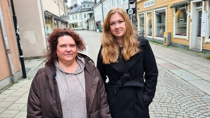 Två kvinnor i småstadsmiljö, på en stenlagd gata.