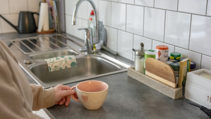 Armen på en person som håller i en kopp på en diskbänk