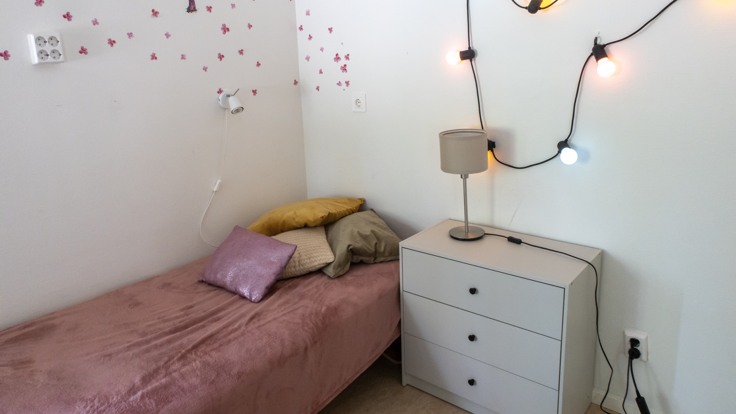 Säng med rosa överkast och ljusslinga på väggen