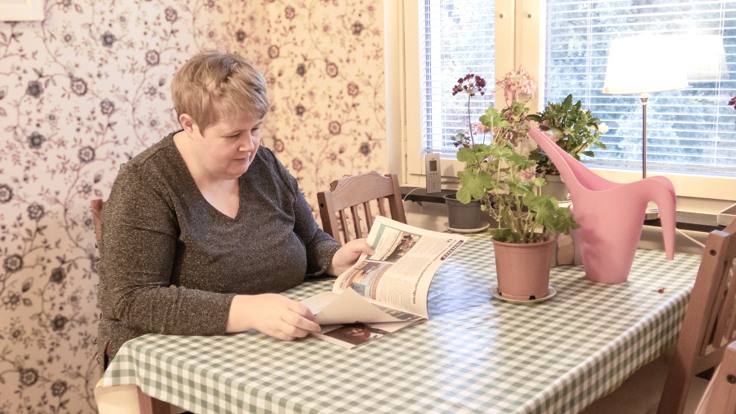 Kvinna som sitter vid ett köksbord och läser en tidning