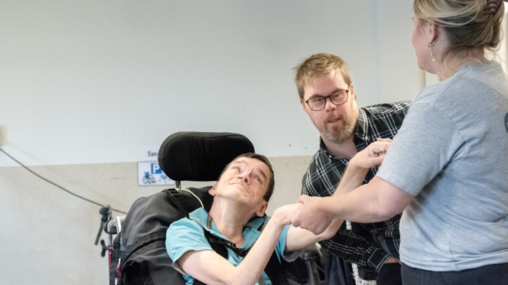 Man i rullstol håller personal i händerna och dansar