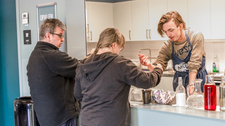 Två kunder som handlar vid cafédisk. En deltagare servar. 