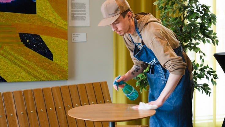 Kille som torkar av bord i café