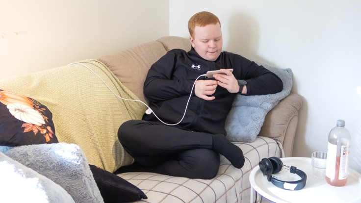 Kille som sitter med en mobiltelefon i en soffa