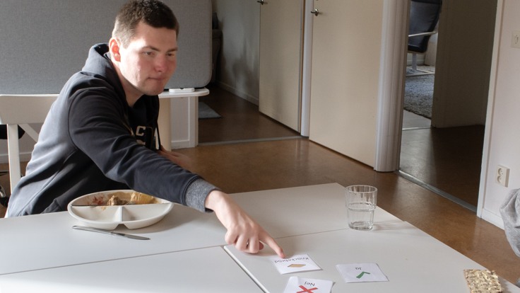 Man som sitter vid ett matbord och pekar på ett bildstödskort