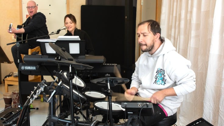 Kille som spelar trummor, två andra musiker i bakgrunden