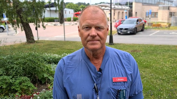 Man i sjukvårdskläder framför sjukhusbyggnad.